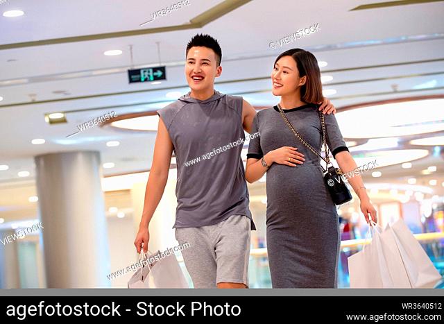 Her husband with his pregnant wife shopping at the mall