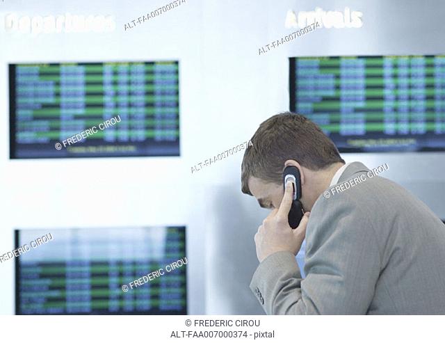 Businessman phoning in front of departure board