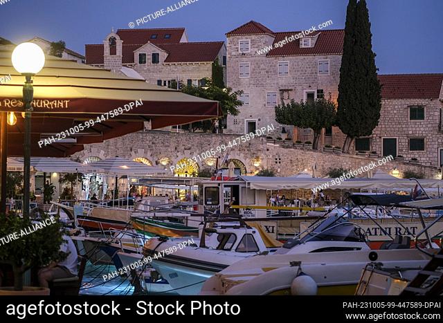 PRODUCTION - 28 September 2023, Croatia, Bol: The harbor with boats, cafes and restaurants in Bol on the island of Brac in the evening