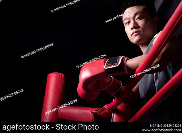 Portrait of male boxer resting his elbows on the ring side, looking at camera, low angle view