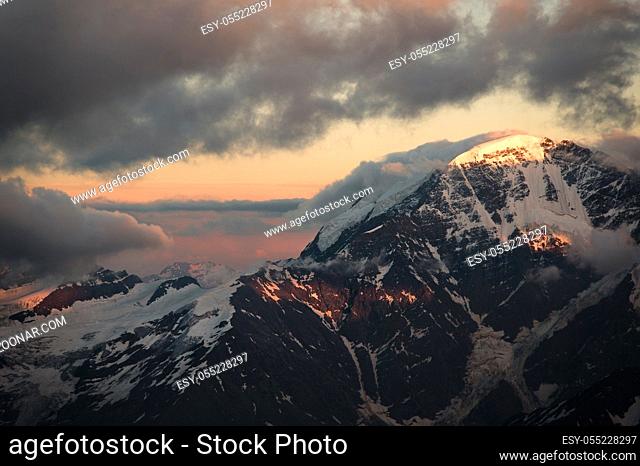A sunset panorama of the elbrus and part of the Caucasian ridge with orange clouds and a cracked glacier at the bottom