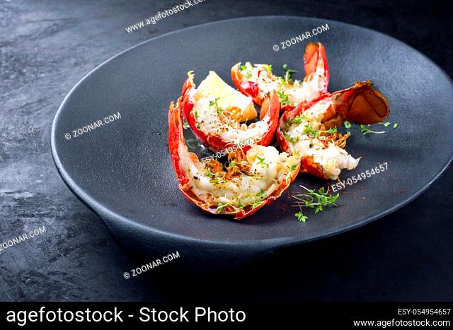 Traditional barbecue spiny lobster tail sliced and offered with lemon slice and herbs as closeup on a modern design plate