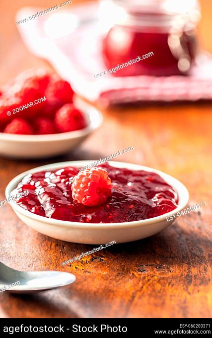 Red rasberries jam in bowl and ripe raspberries on wooden table