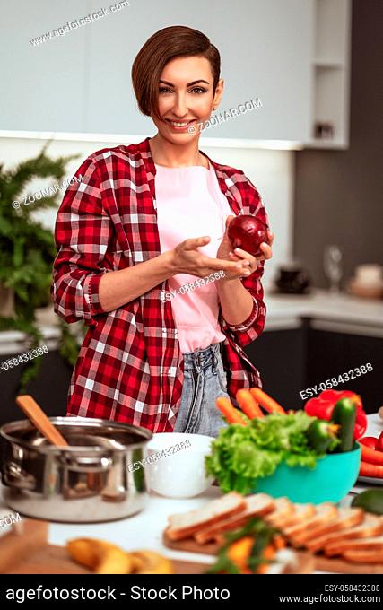 Housewife prepares dinner for family choosing a vegetables holding a red onion in a hands standing in the kitchen. Healthy food at home