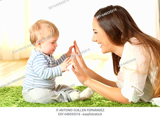 Side view portrait of a happy mother playing with her baby touching hands on a carpet at home