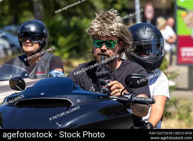 24 July 2022, Saxony, Dresden: A man has a glove in his mouth and artificial hair on his head. This takes part in the biker parade through downtown Dresden