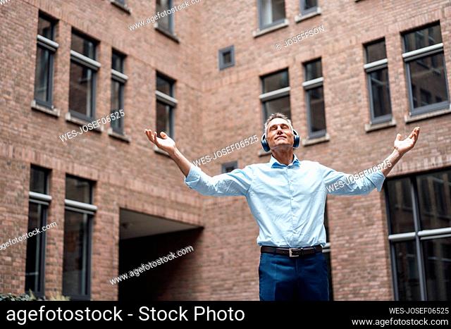 Mature businessman with eyes closed enjoying music in front of office building