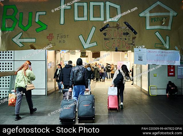 09 March 2022, Berlin: A huge makeshift banner with the words ""Bus"", ""Food"" and a house on it hangs in the main train station to show refugees the way