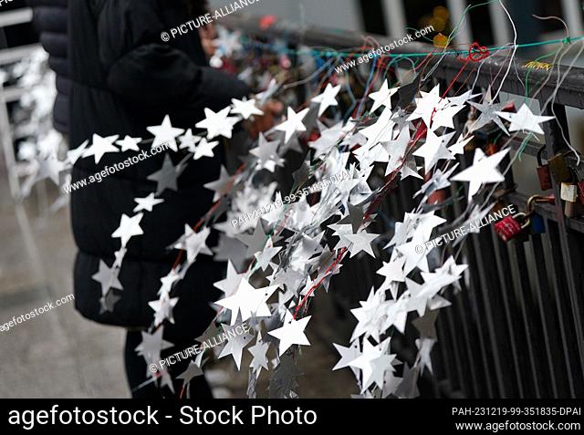 19 December 2023, Hamburg: Schoolgirls attach homemade stars made from the aluminum lids of yogurt and pudding cups to the Michaelis Bridge in the city center