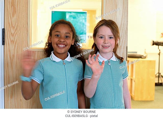 Portrait of two schoolgirls waving in primary school