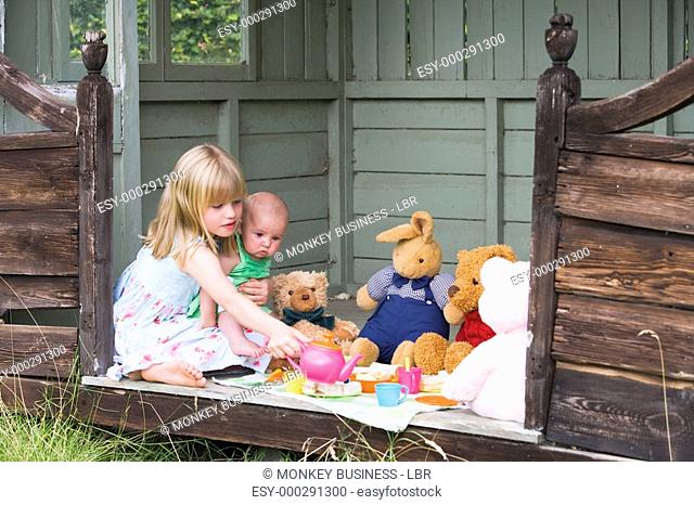 Young girl in shed with baby playing tea