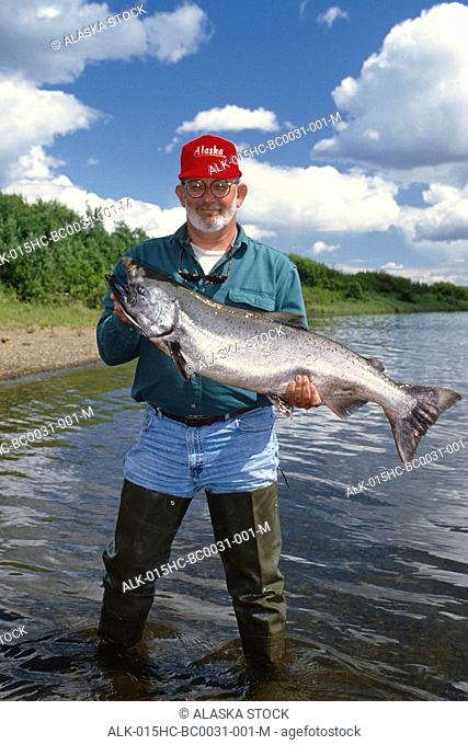 Fisherman holding large king salmon along shoreline Nushagak River Southwest AK Summer