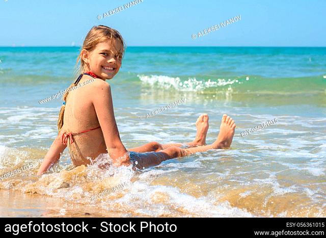 Happy girl sitting on a sandy beach and looking back smiling looked into the frame