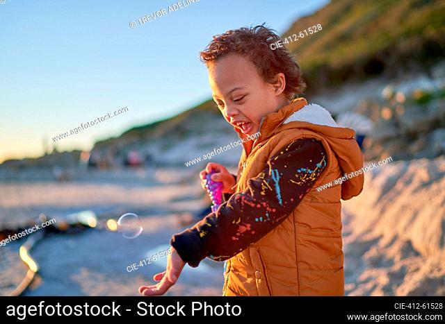 Cute boy with Down Syndrome playing with bubbles on beach