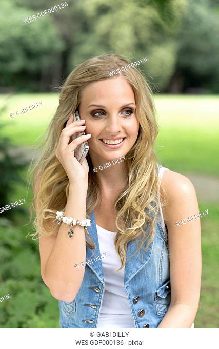 Germany, Oberhausen, Young woman talking on mobile phone, smiling