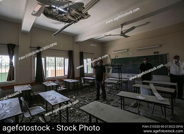 30 May 2021, Palestinian Territories, Gaza City: An employee of the Palestinian Ministry of Education inspects a hole in the ceiling of a damaged classroom at a...