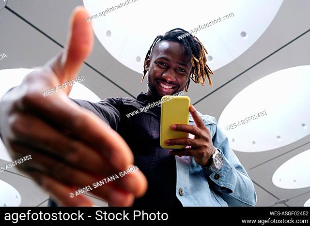 Smiling man with smart phone gesturing by illuminated ceiling