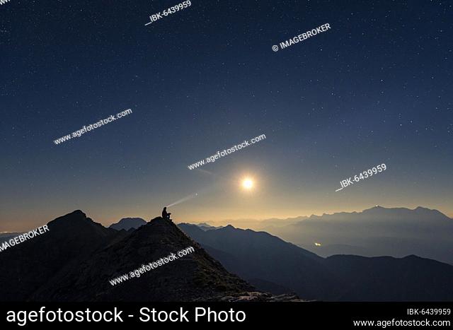 Mountaineer on summit ridge with full moon and starry sky, in the background Ammergau Alps, Reutte, Ammergau Alps, Tyrol, Austria, Europe