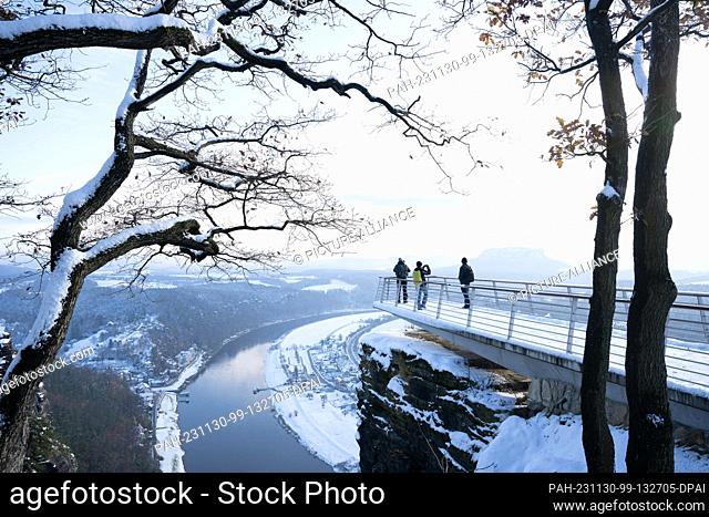 30 November 2023, Saxony, Lohmen: Passers-by stand on a viewing platform on the Bastei rock in the snow-covered Saxon Switzerland National Park