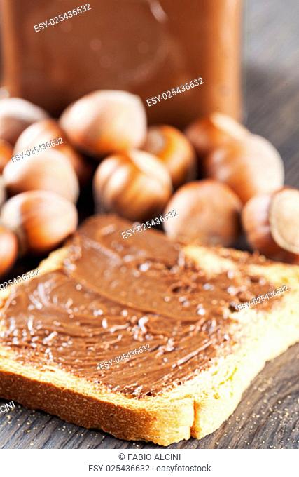 Chocolate over rusk, with hazelnuts and jar on the background, focus on first part of rusk, vertical image