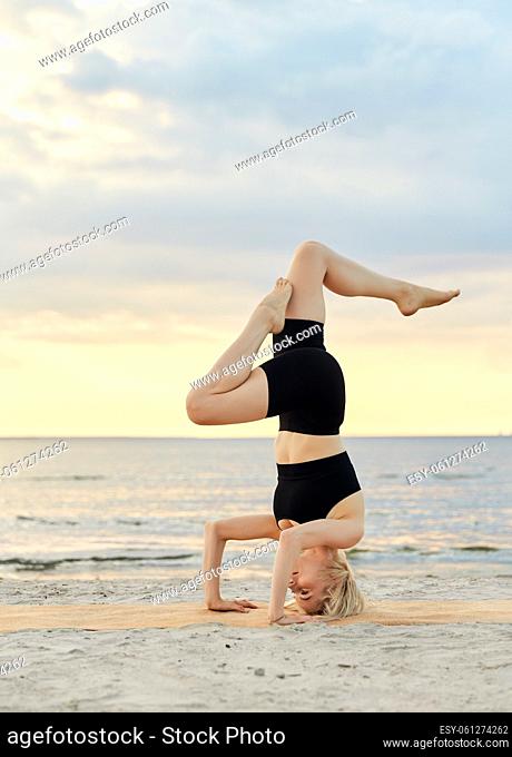 woman doing yoga headstand on beach