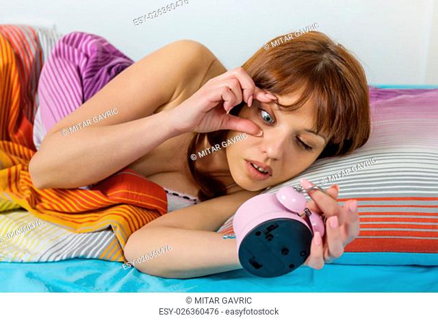 Oversleeping woman looking on the alarm clock
