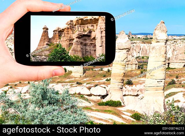 travel concept - tourist photographs of landscape with old fairy chimney rocks in mountains of Goreme National Park in Cappadocia on smartphone in Turkey in...