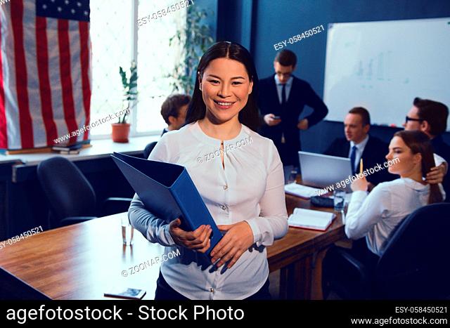 Business Woman Holding Folder While Standing Middle Office. Her Colleagues On Background
