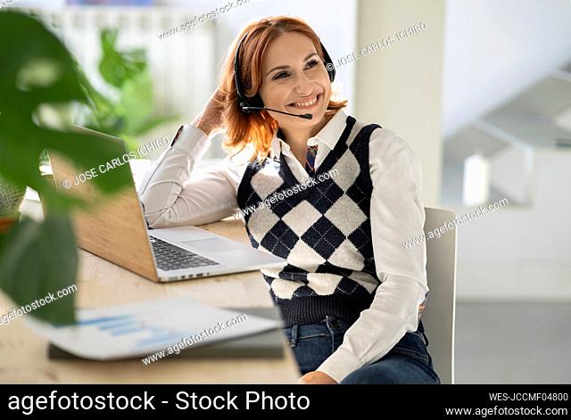 Businesswoman with headset sitting at desk with laptop in home office