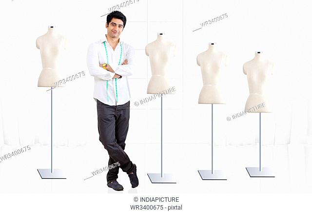 Full length of young male fashion designer standing by mannequin at studio