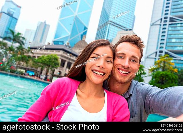 Selfie tourists couple Asian woman and Caucasian taking picture with phone in Hong Kong city, Asia travel lifestyle. Two people taking a self potrait photo