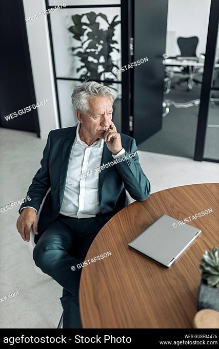 Thoughtful businessman sitting on chair by table at office