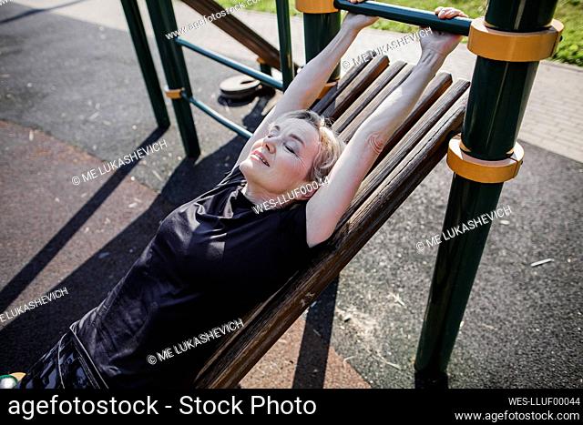 Woman exercising while lying on gym equipment at park