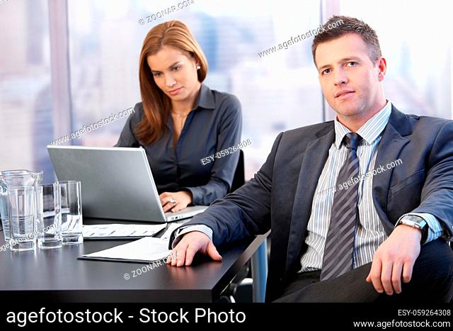 Boss and assistant sitting at table in meeting room, working
