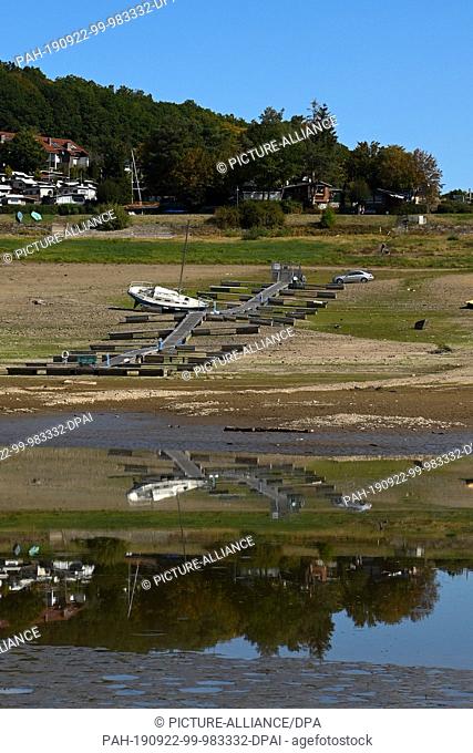 22 September 2019, Hessen, Bringhausen: A dry fallen sailboat is reflected near Scheid in the last bit of Edersee, which here has only the width of the river...