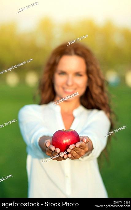 Pretty woman showing red apple. Girl with long brown hair keeping an apple in front of her