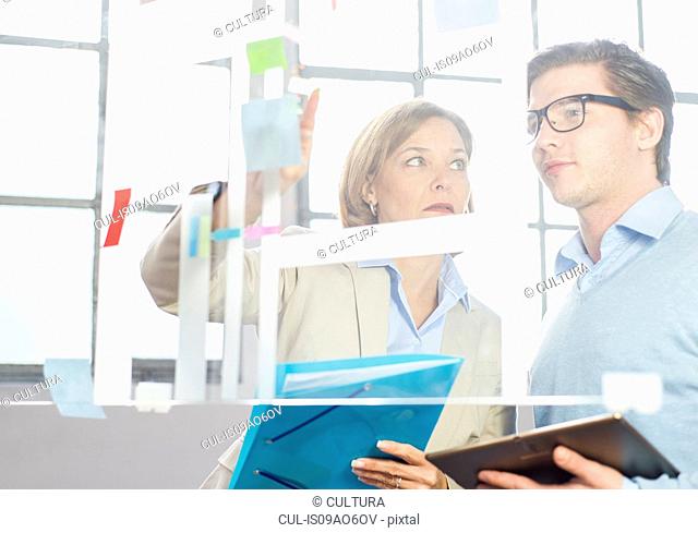 Businessman and woman pointing at idea notes on office glass wall