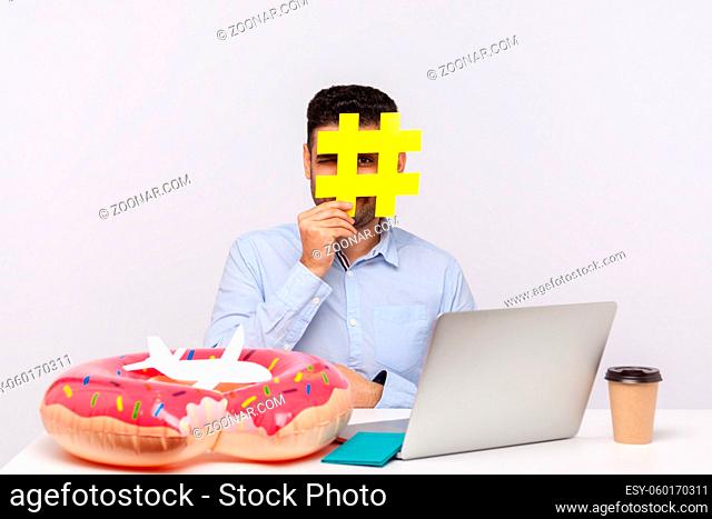 Time to rest. Man looking through hashtag symbol, sitting in office workplace with rubber ring passport and paper airplane on desk