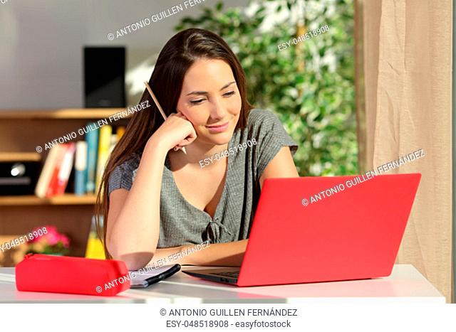 Studious student e-learning at home using a red laptop