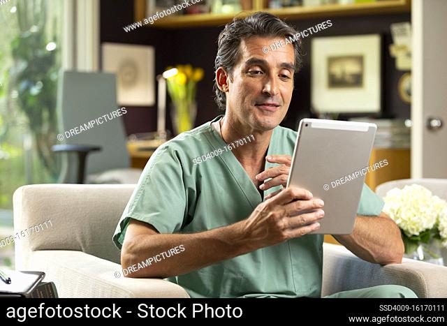 Hispanic Male doctor practicing tele-medicine from his home office, Talking to patient via video call on tablet