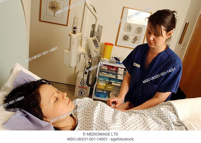 A nurse prepares a woman patient for an intravenous line IV injection, against a background of monitoring equipment