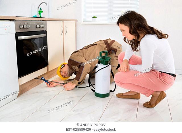 Young Woman And Worker With Pesticide Sprayer In Kitchen At Home