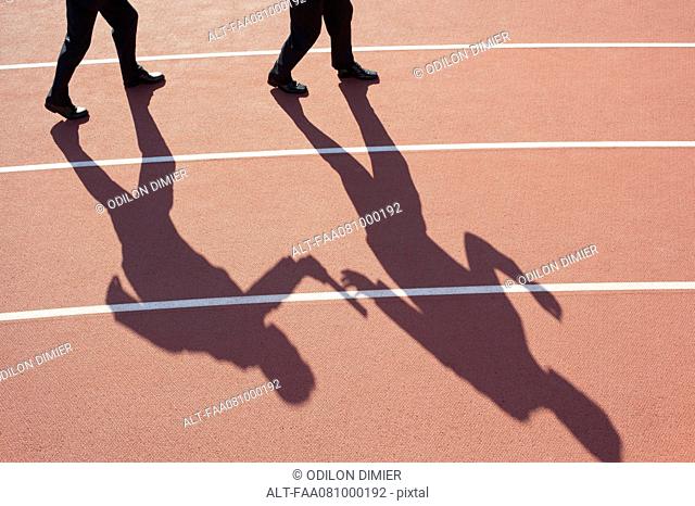 Shadow of men passing baton on running track