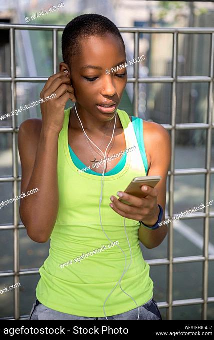 Woman adjusting headphones by metal fence