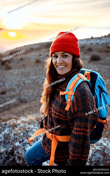 Happy female hiker with backpack standing on mountain during sunset