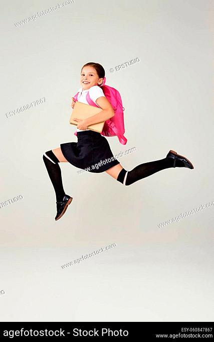 cute schoolgirl jumping up with pink backpack isolated on gray background. happy child is ready to learn. Back to school