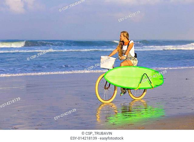 Young girl with surfboard and bicycle on the beach