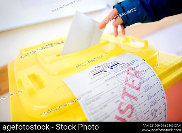 09 October 2022, Lower Saxony, Hanover: A voter throws her ballot paper into a ballot box in a voting room at the Lutherschule