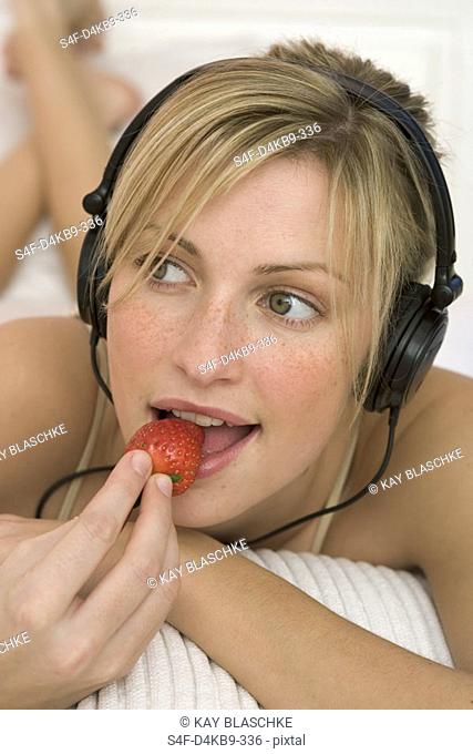 Woman listening to music by earphones, eating a strawberry