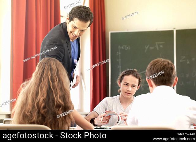 Teacher standing while math lesson in front of a blackboard and educate or teach students or pupils or mates in a school or class